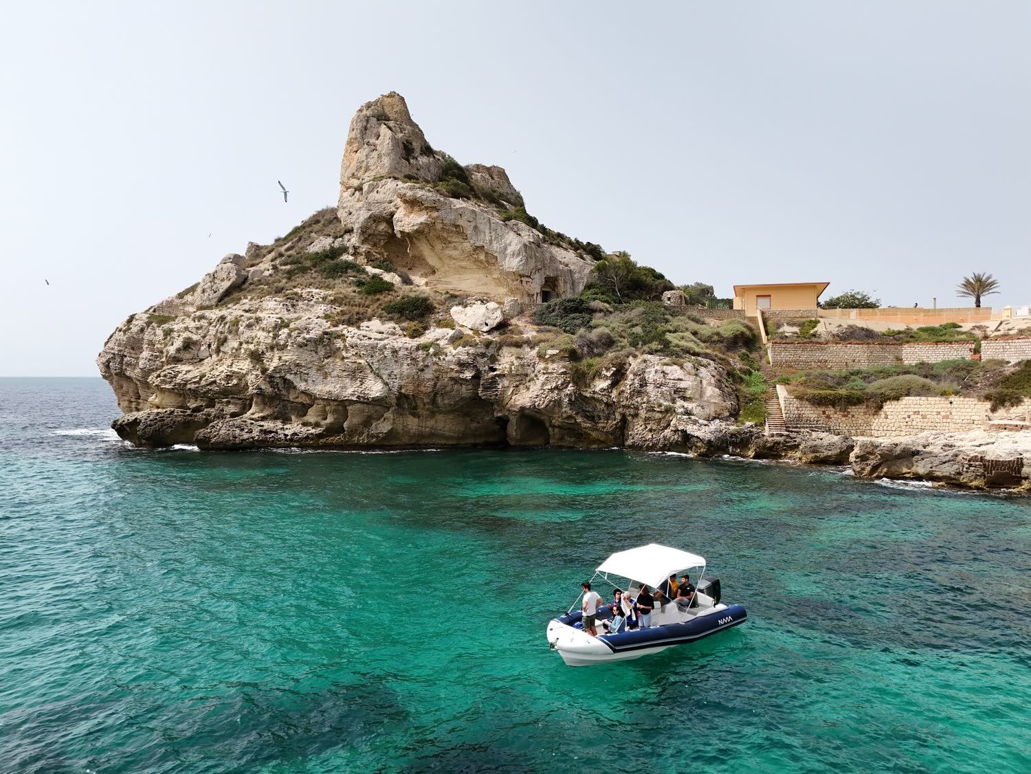 Gommone da noleggio fermo sull'acqua turchese accanto allo scoglio, visto dall'alto