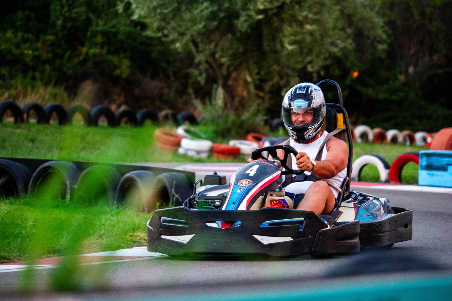 Pilota di kart in curva, ripreso attraverso l'erba in primo piano